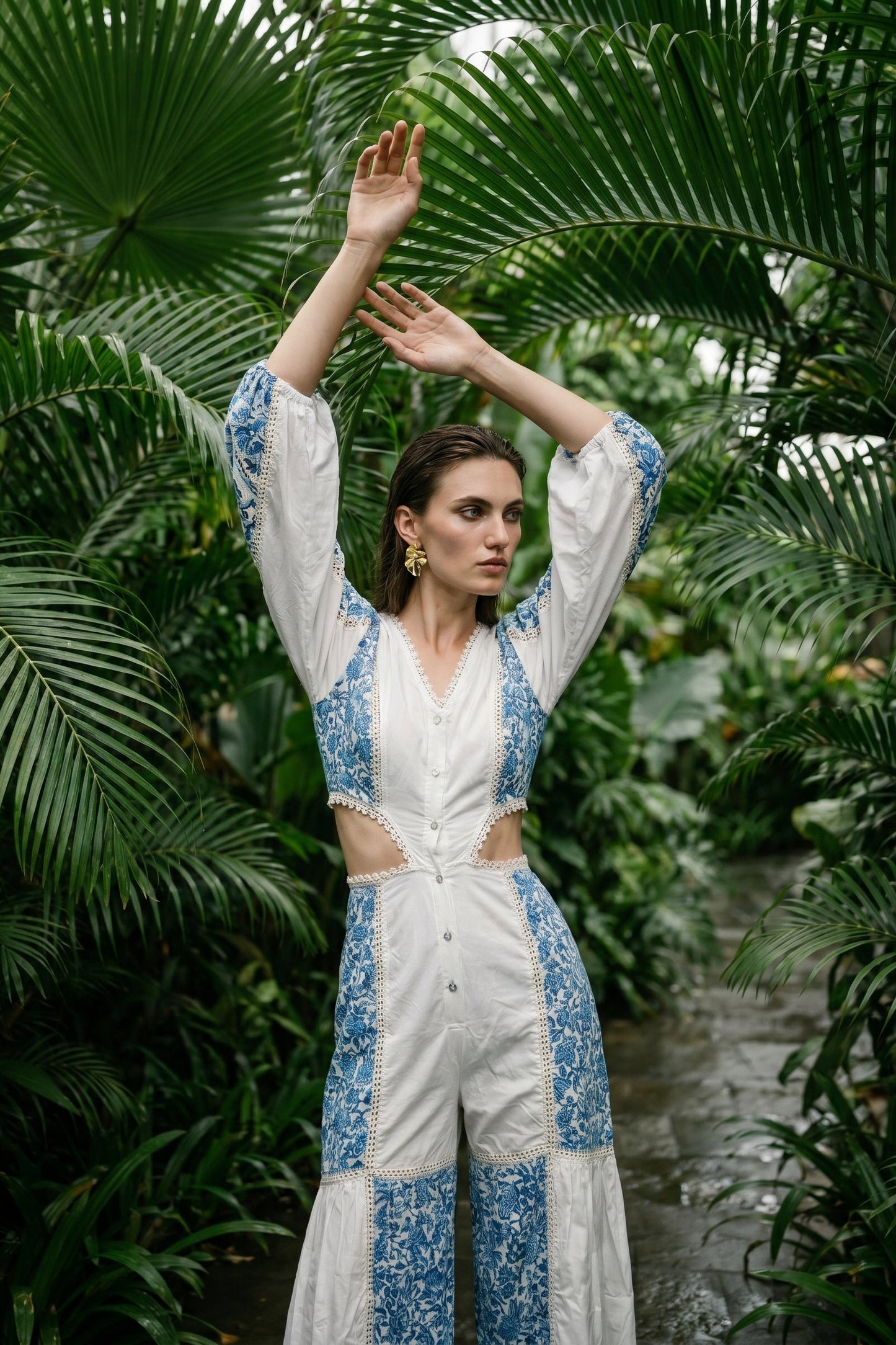 Woman in a white and blue floral outfit standing among tropical plants.