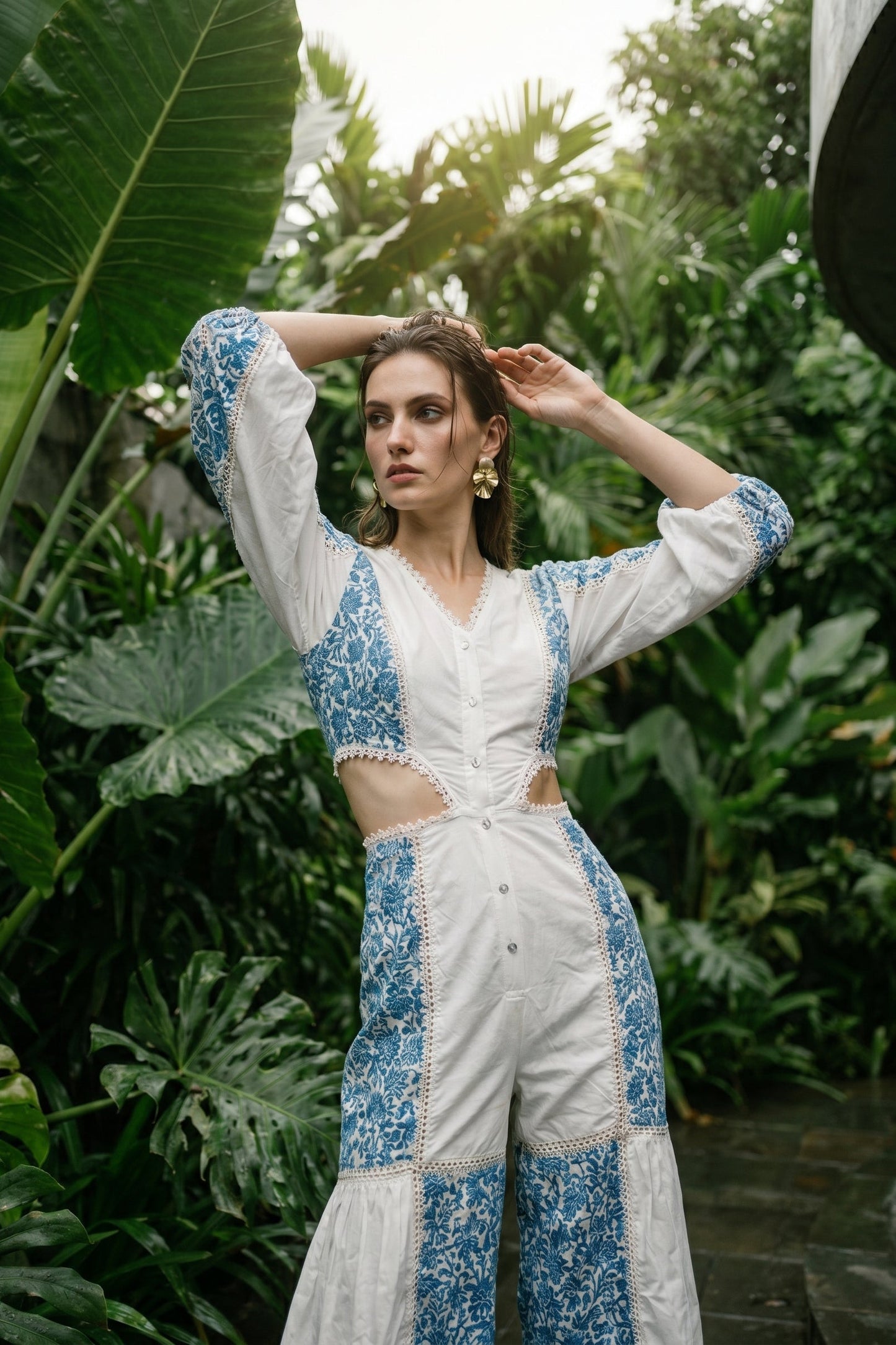 Woman in a white and blue floral outfit standing in a lush green garden.