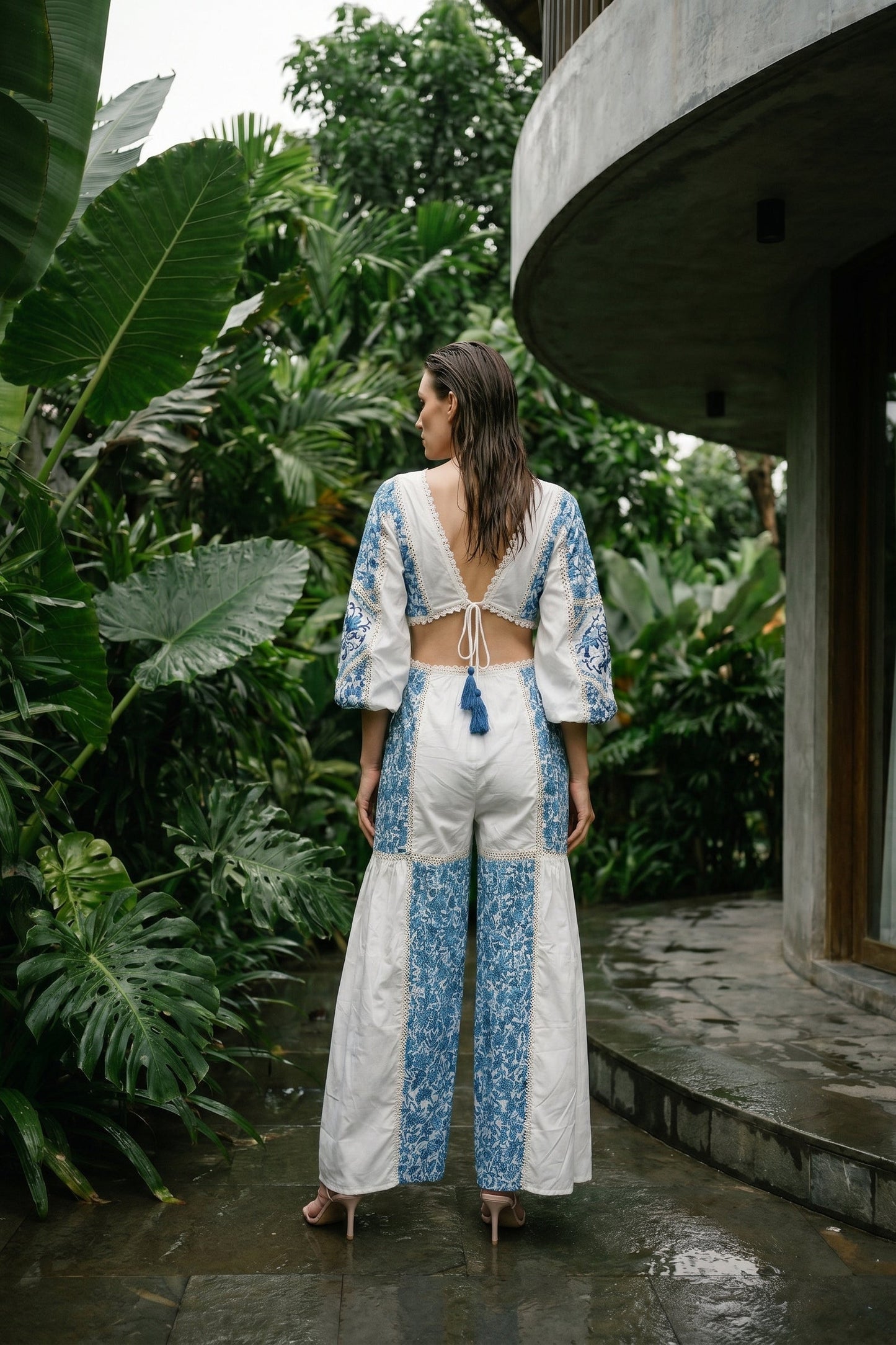 Woman in a white and blue outfit standing in a lush green garden.