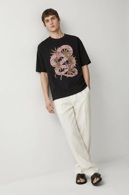Man wearing a black t-shirt with a pink and gold graphic design and white pants on a light gray background
