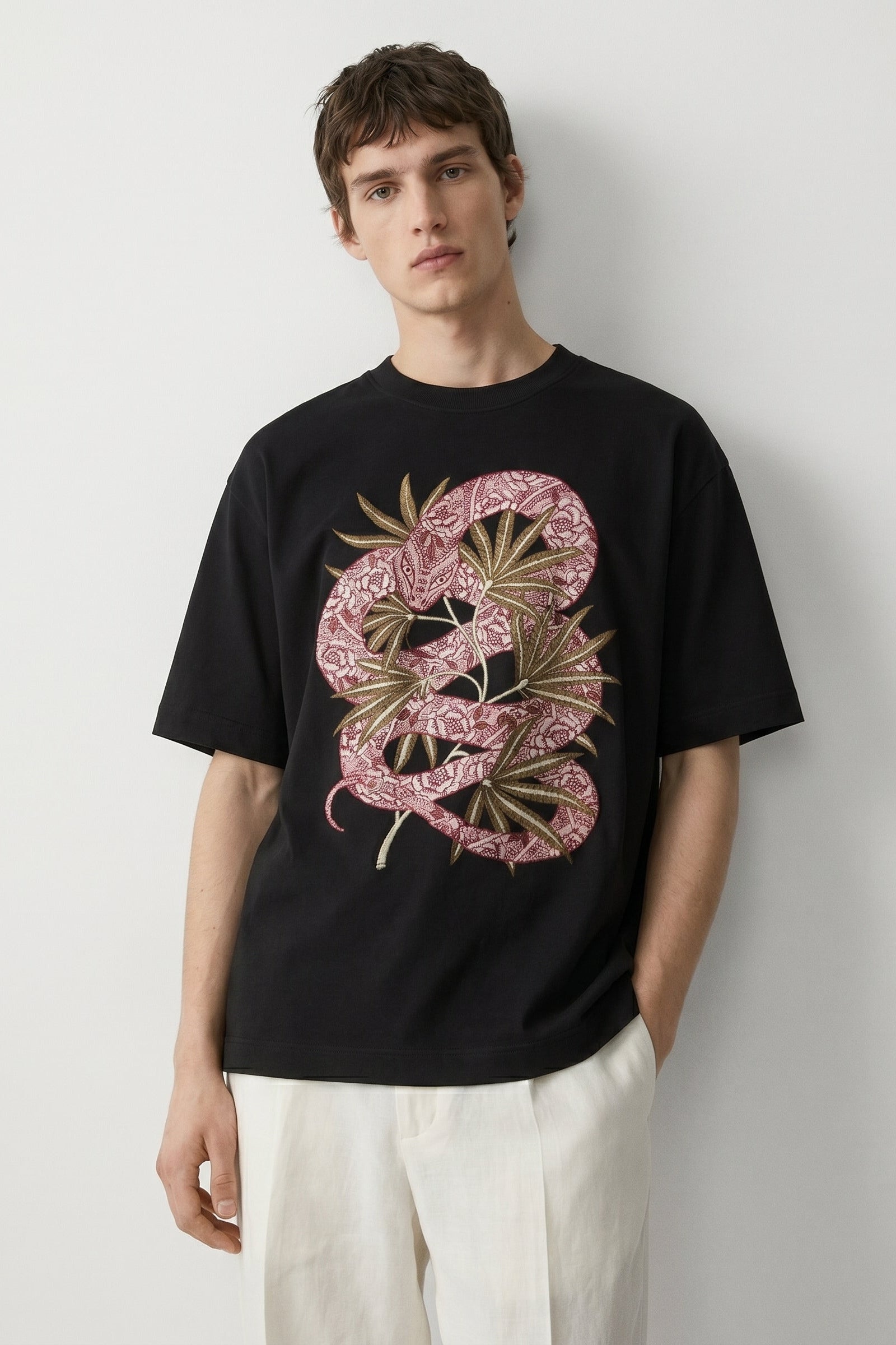 Person wearing a black t-shirt with a pink and gold snake design on a plain background