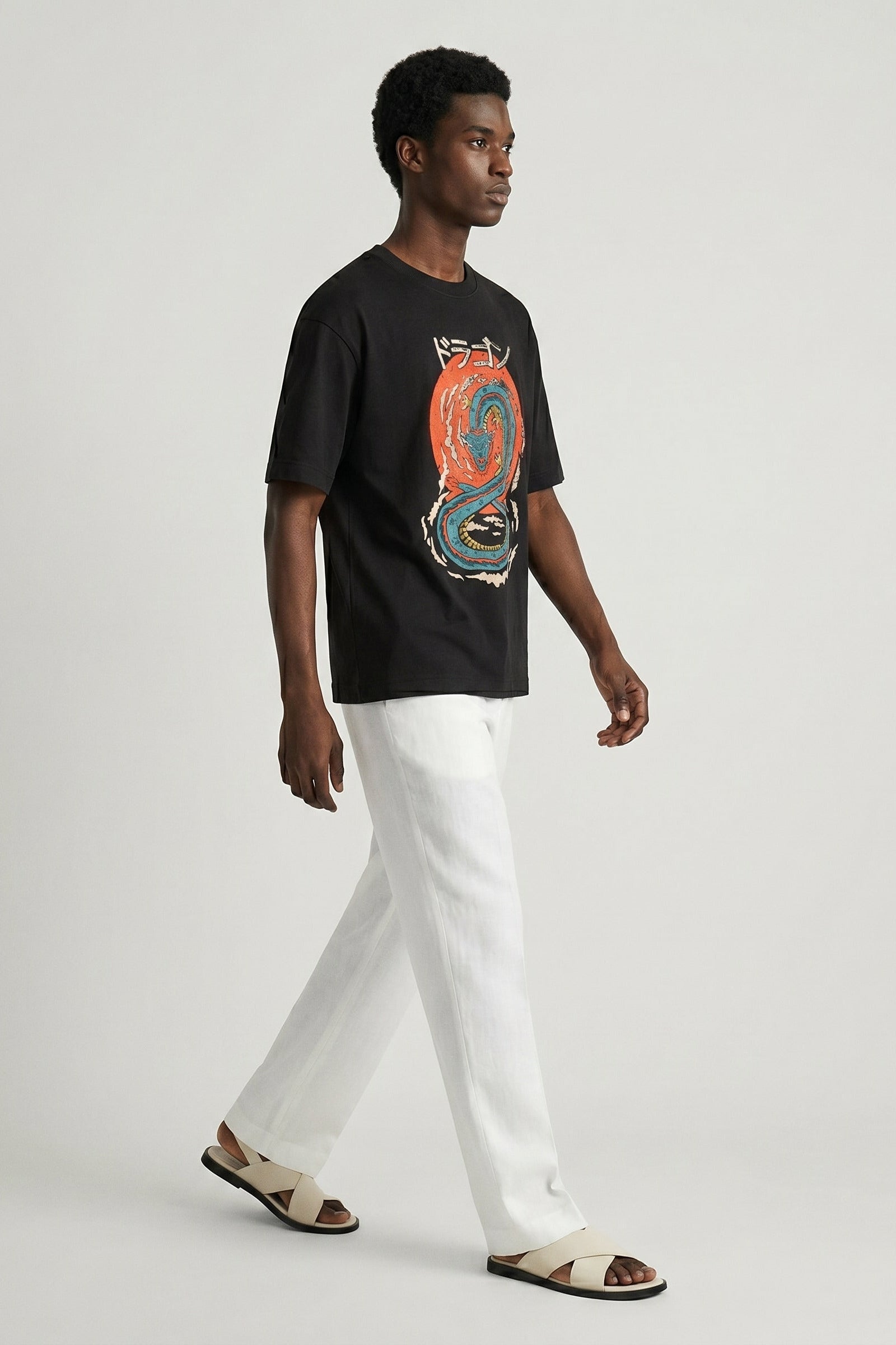 Man wearing a black t-shirt with a colorful graphic design and white pants on a light gray background