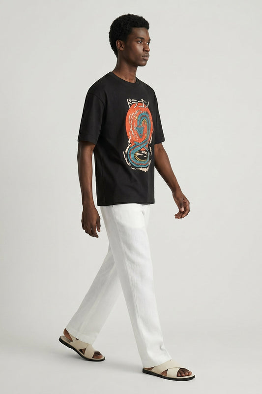 Man wearing a black t-shirt with a colorful graphic design and white pants on a light gray background