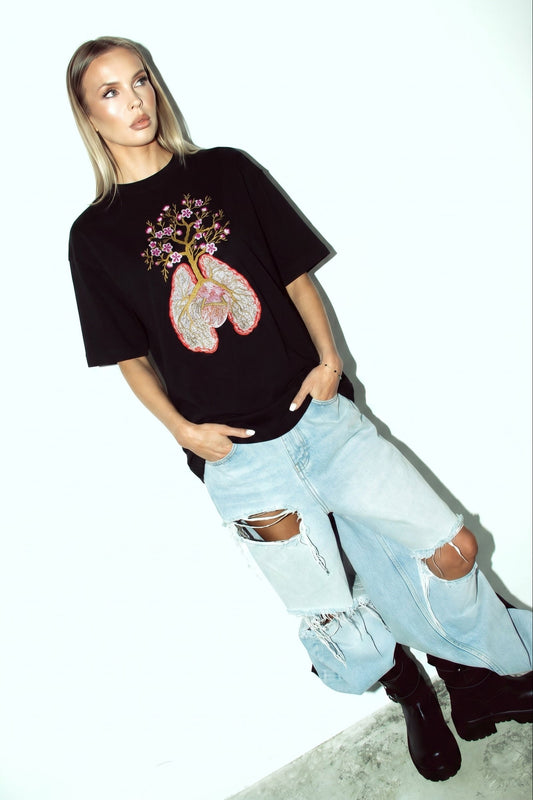 Person wearing a black t-shirt with a floral design and light blue jeans on a white background