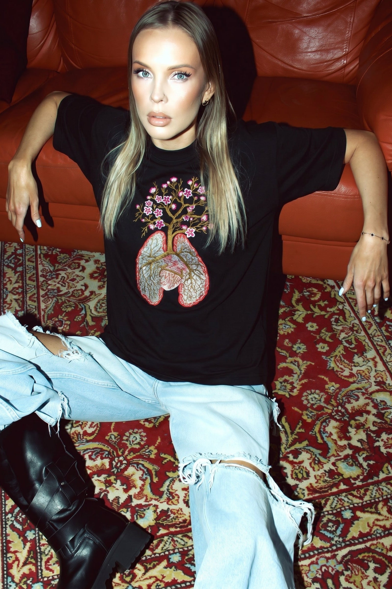 Woman wearing a black t-shirt with a graphic design, sitting on a red leather couch.