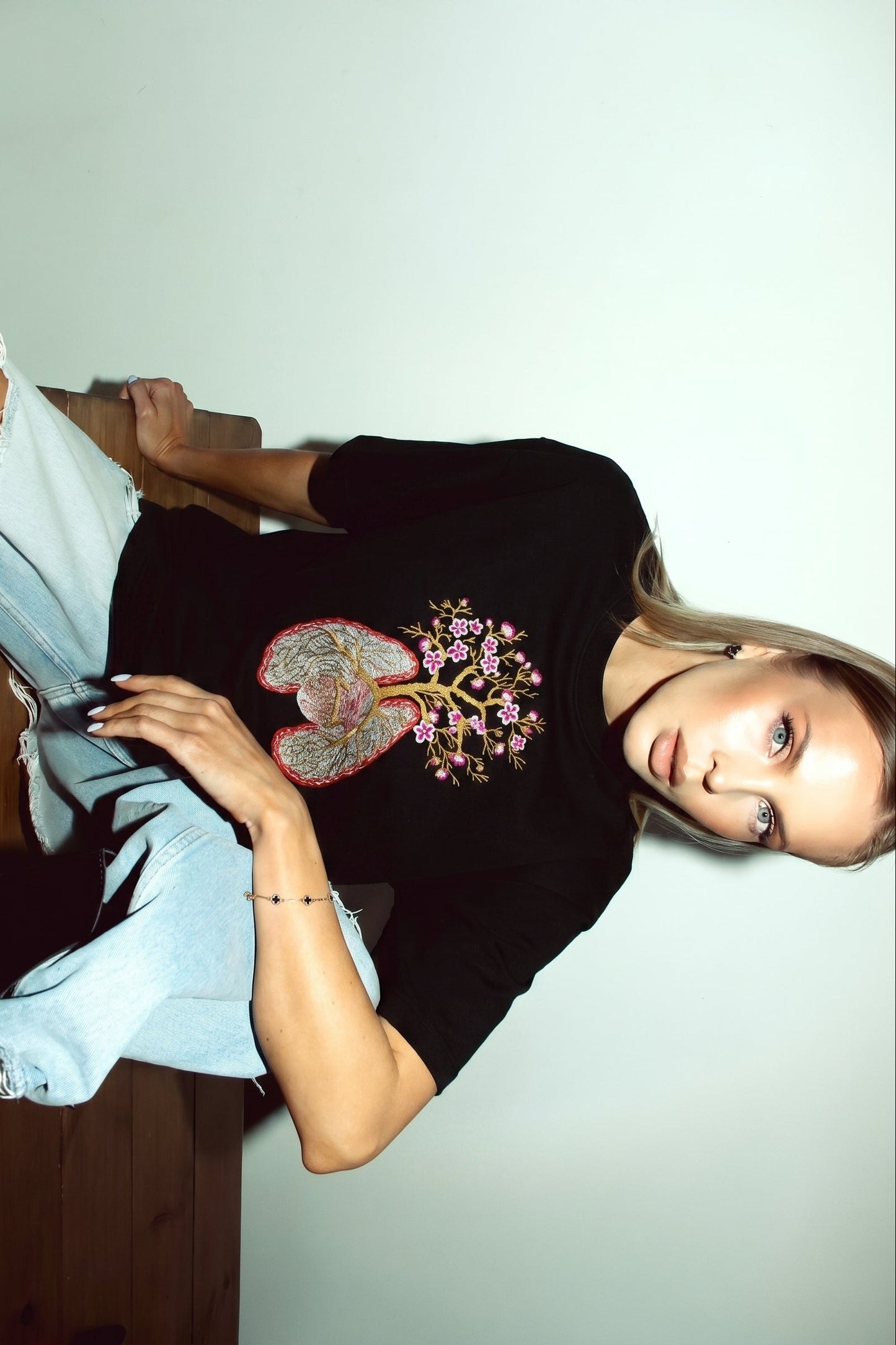 Person wearing a black t-shirt with a colorful design, sitting on a wooden floor.