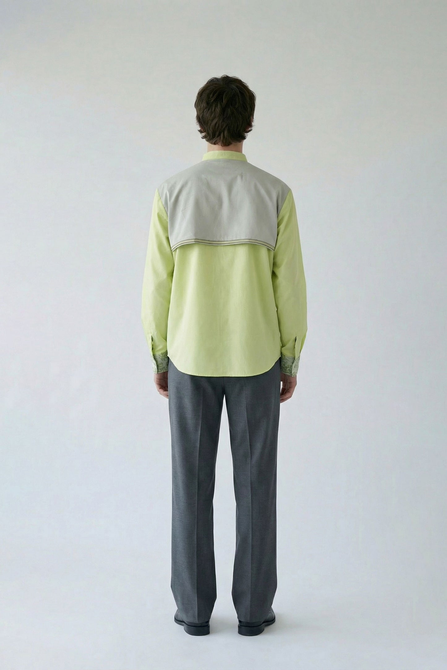 Person wearing a light green shirt with a gray vest and gray pants on a white background