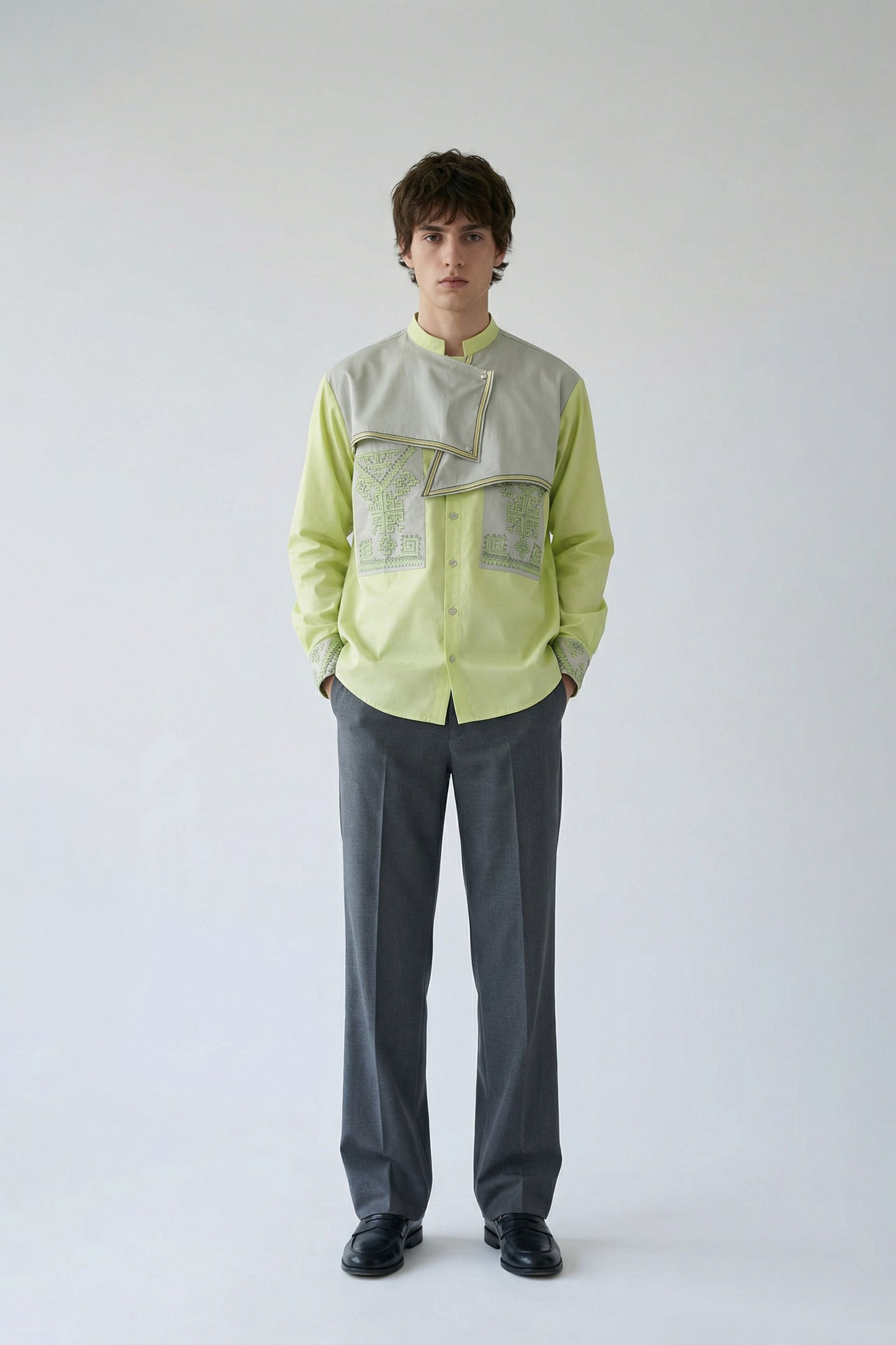 Person wearing a light green shirt with a textured pattern and gray pants on a white background