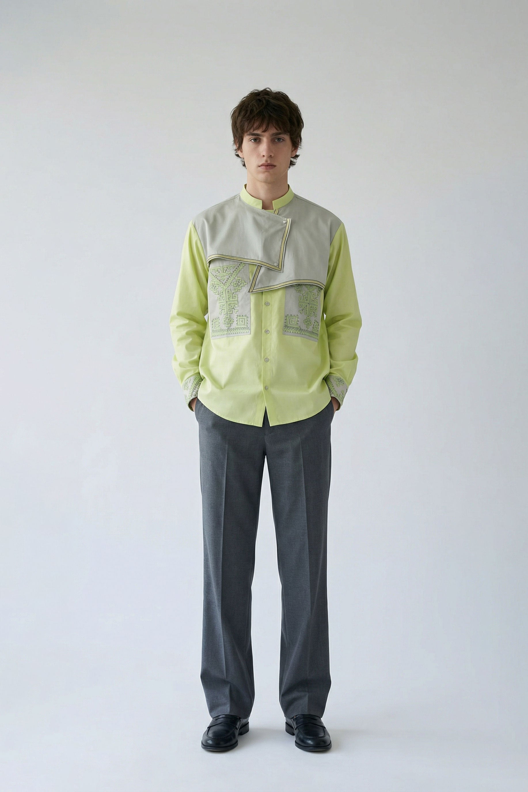 Person wearing a light green shirt with a textured pattern and gray pants on a white background