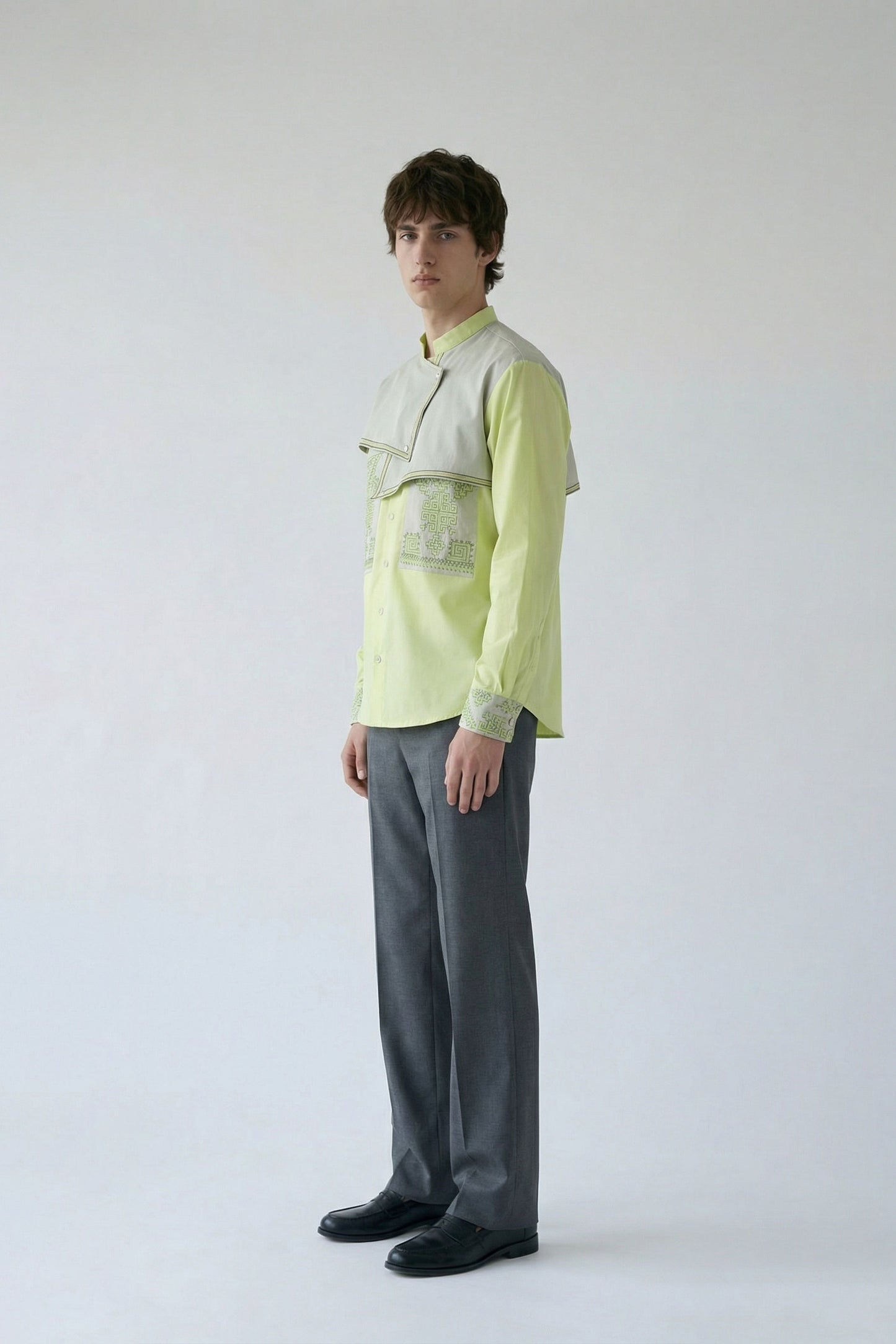 Person wearing a light green shirt with a textured pattern and gray pants on a white background