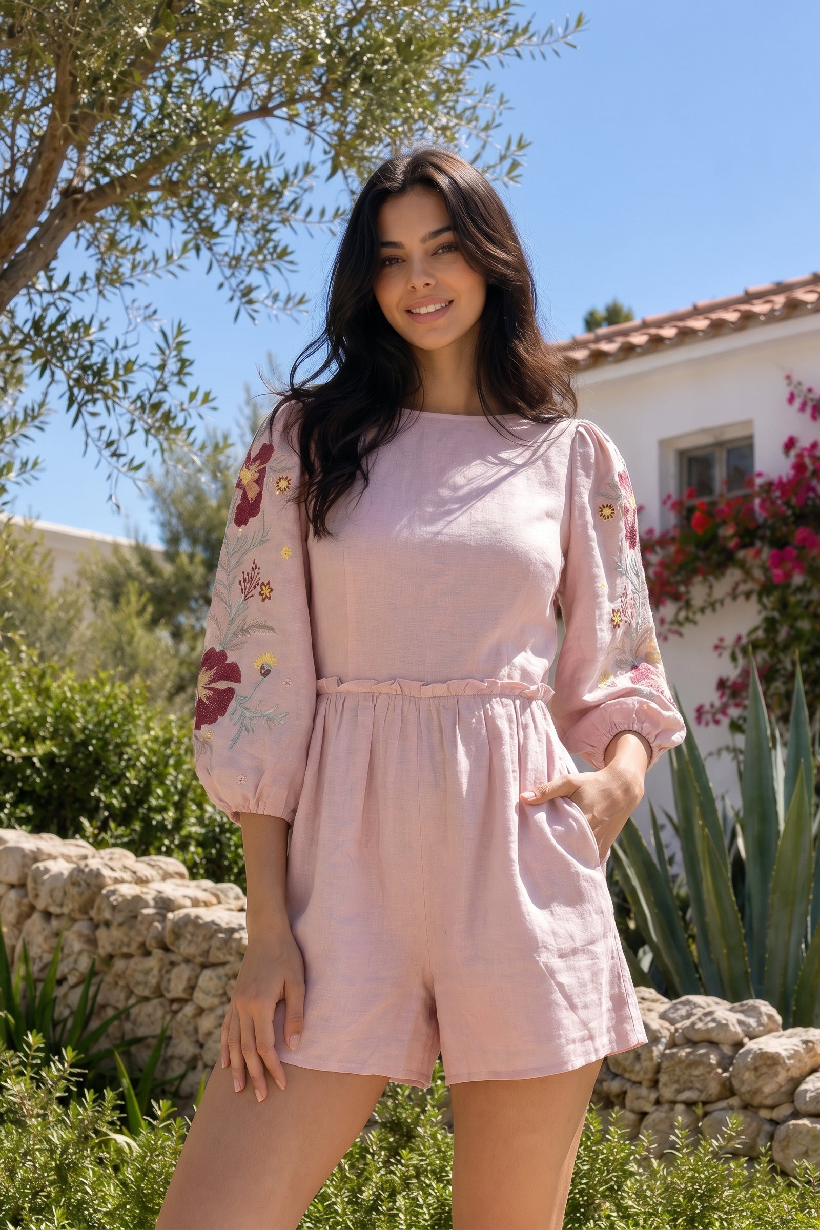 Woman in a pink outfit standing outdoors with greenery and a house in the background
