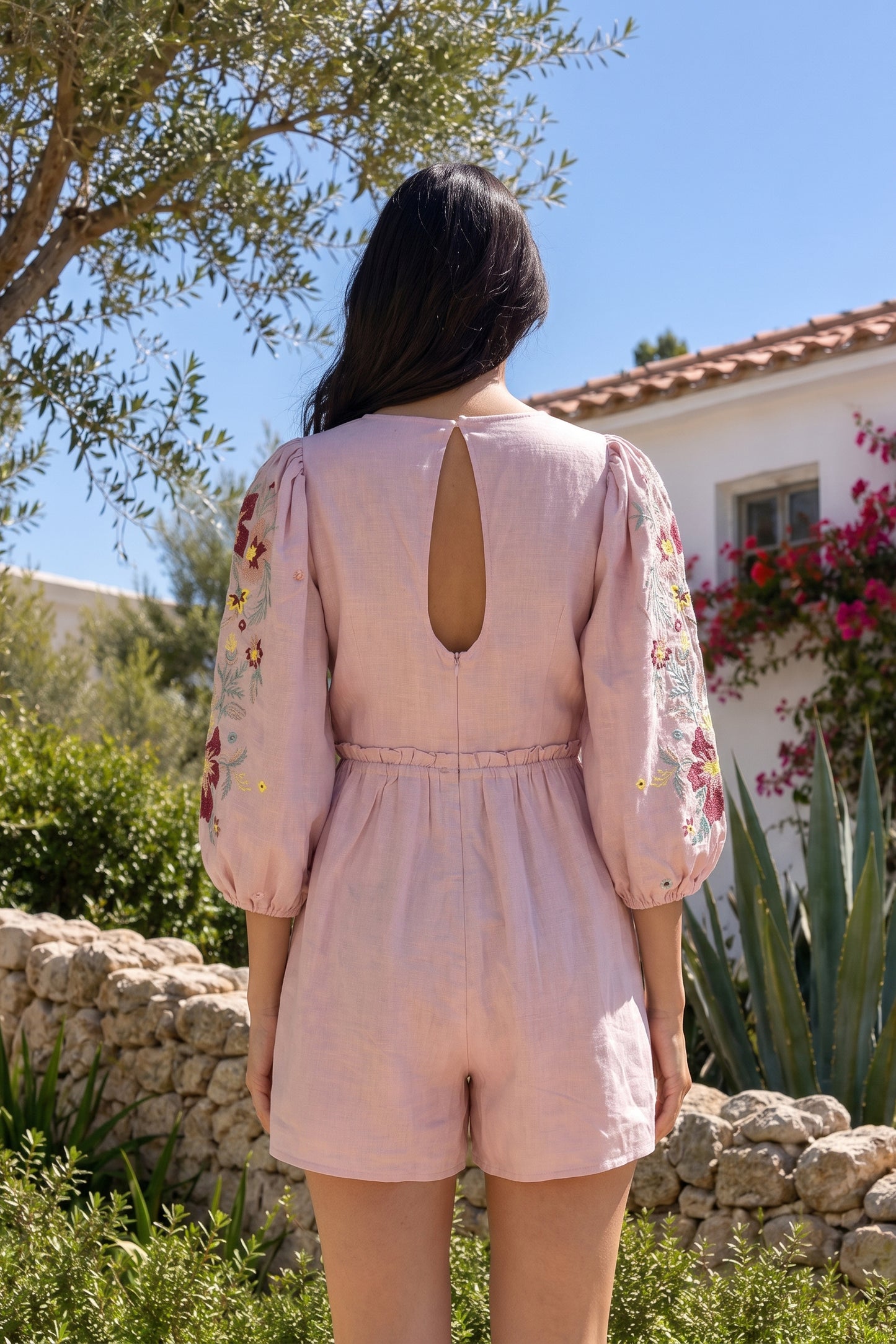 Woman wearing a pink embroidered romper in a garden setting
