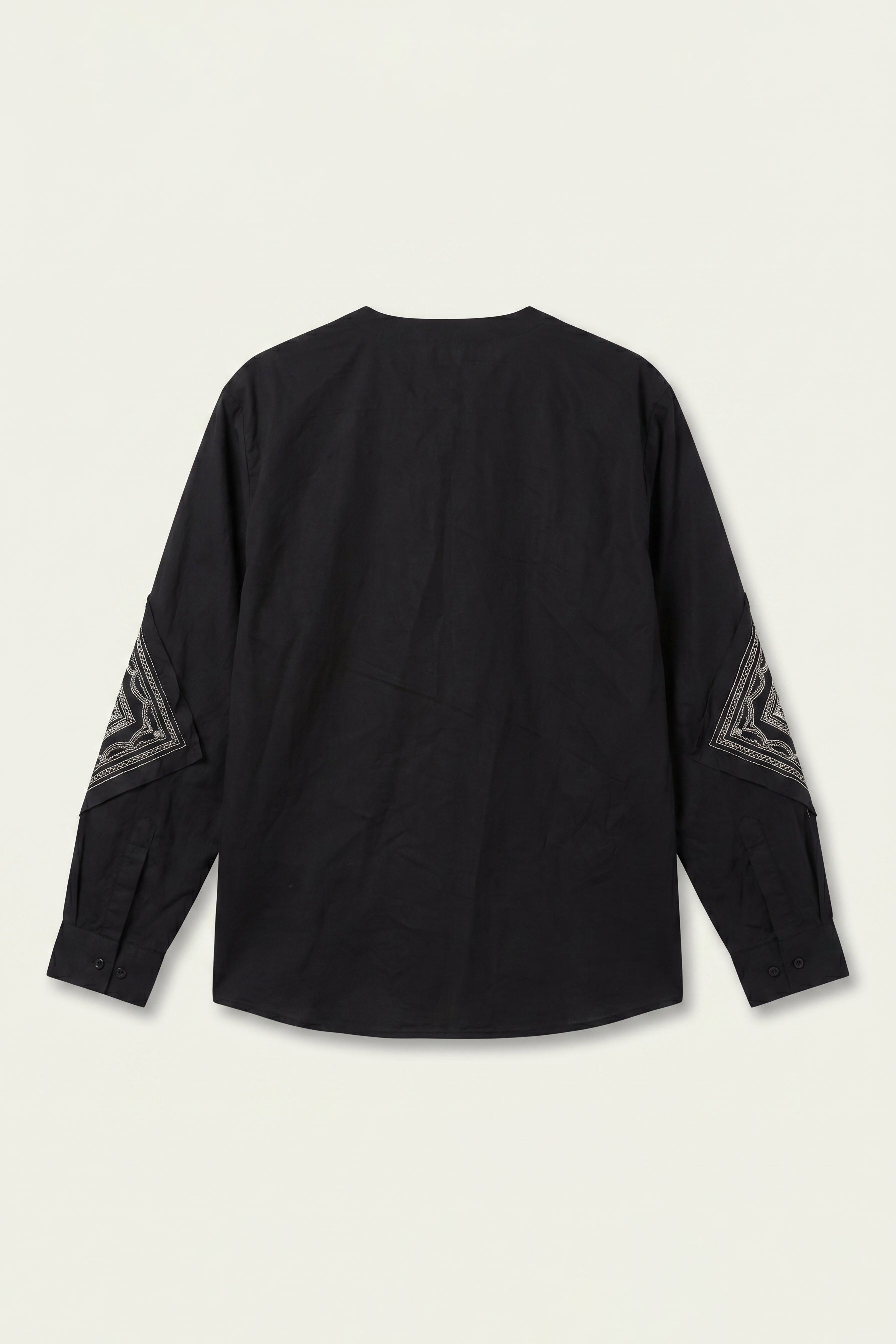 Black long-sleeve top with geometric patterns on sleeves against a beige background