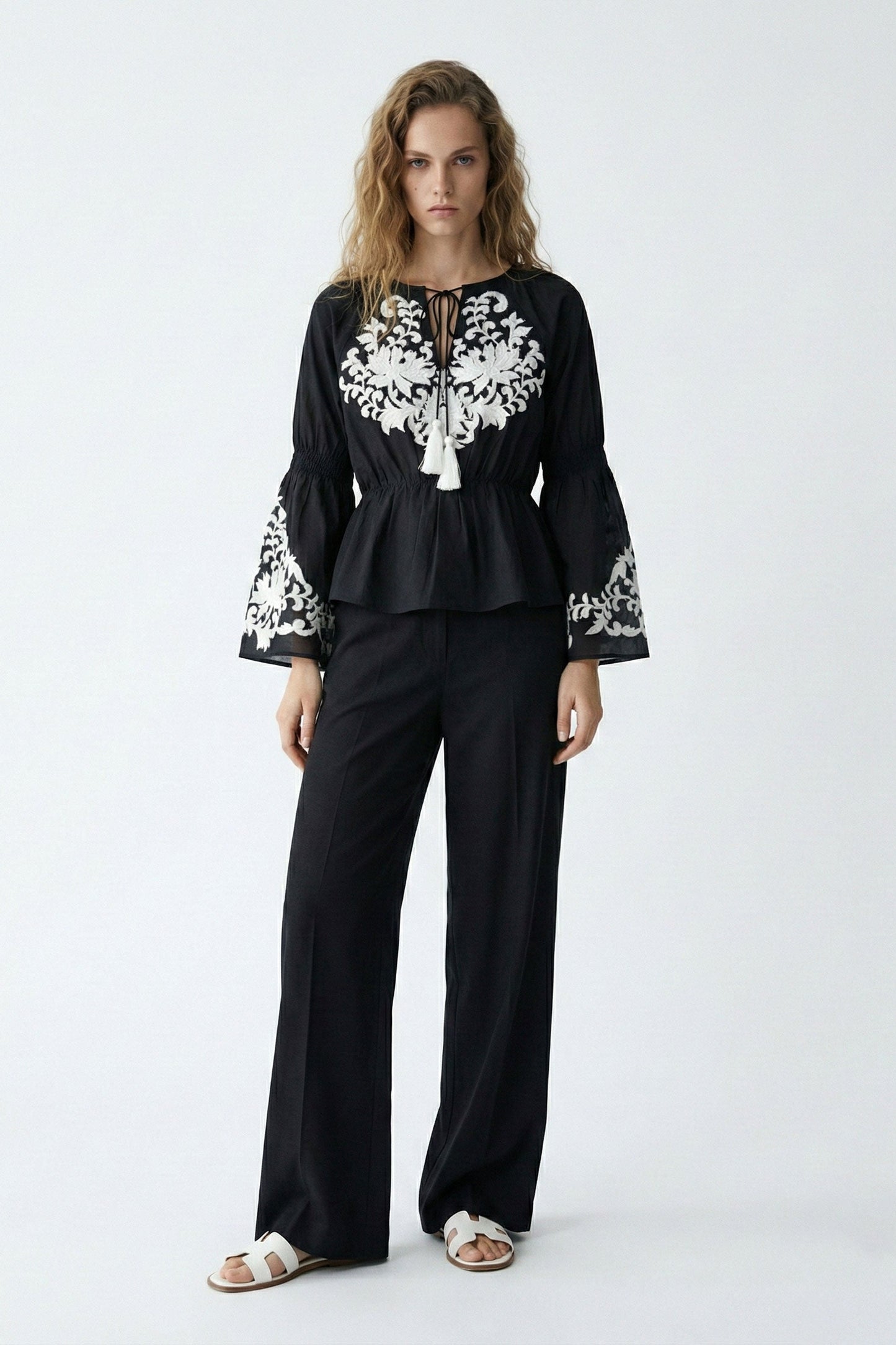 Woman wearing a black outfit with white embroidery on a white background