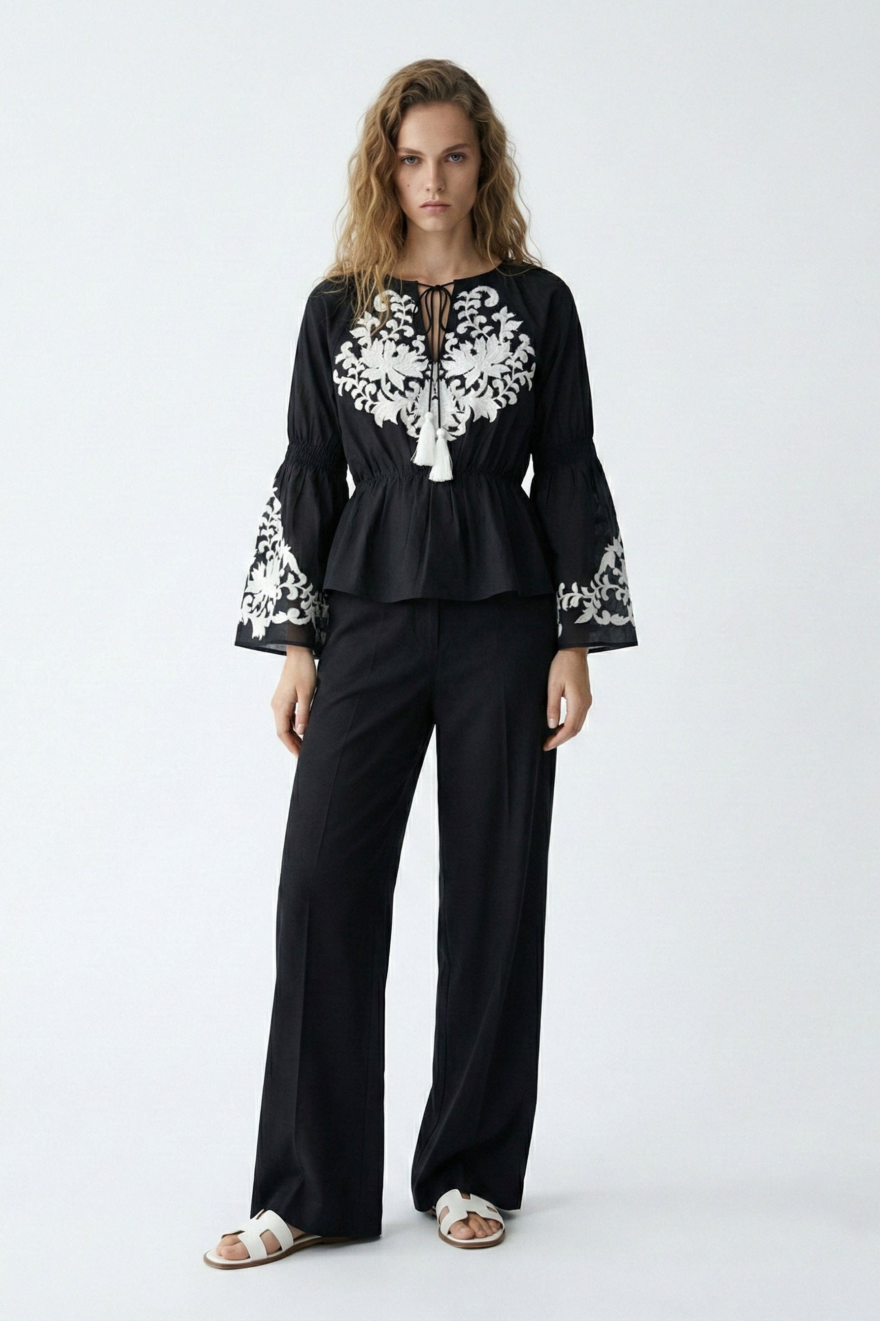 Woman wearing a black outfit with white embroidery on a white background