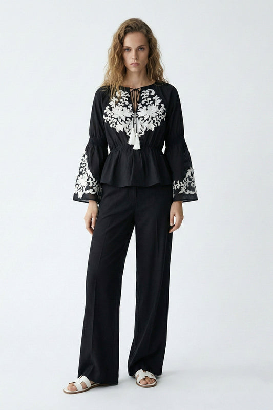 Woman wearing a black outfit with white embroidery on a white background