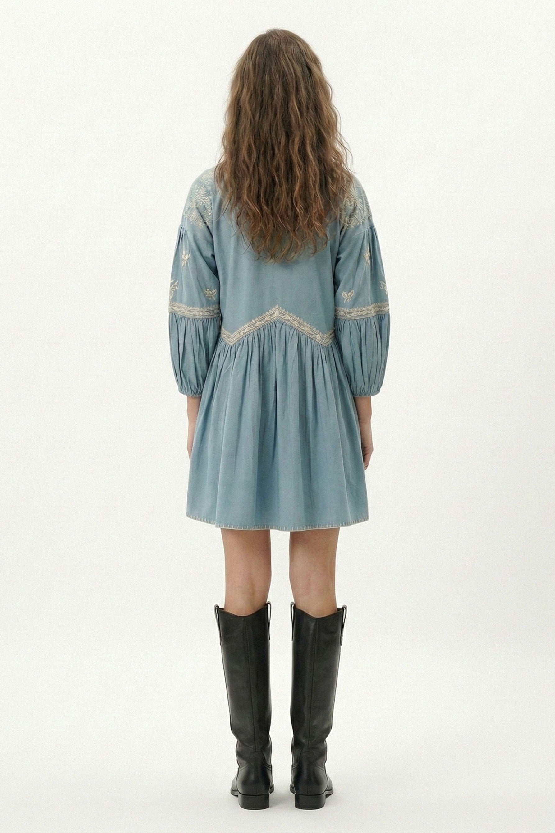 Model wearing a light blue dress with embroidery and black boots on a white background
