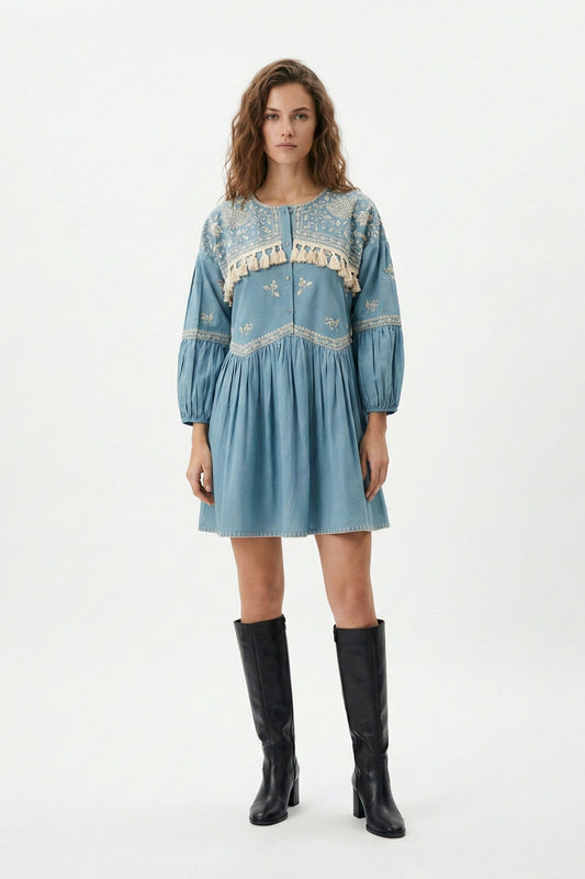 Woman wearing a blue embroidered dress with black boots on a white background