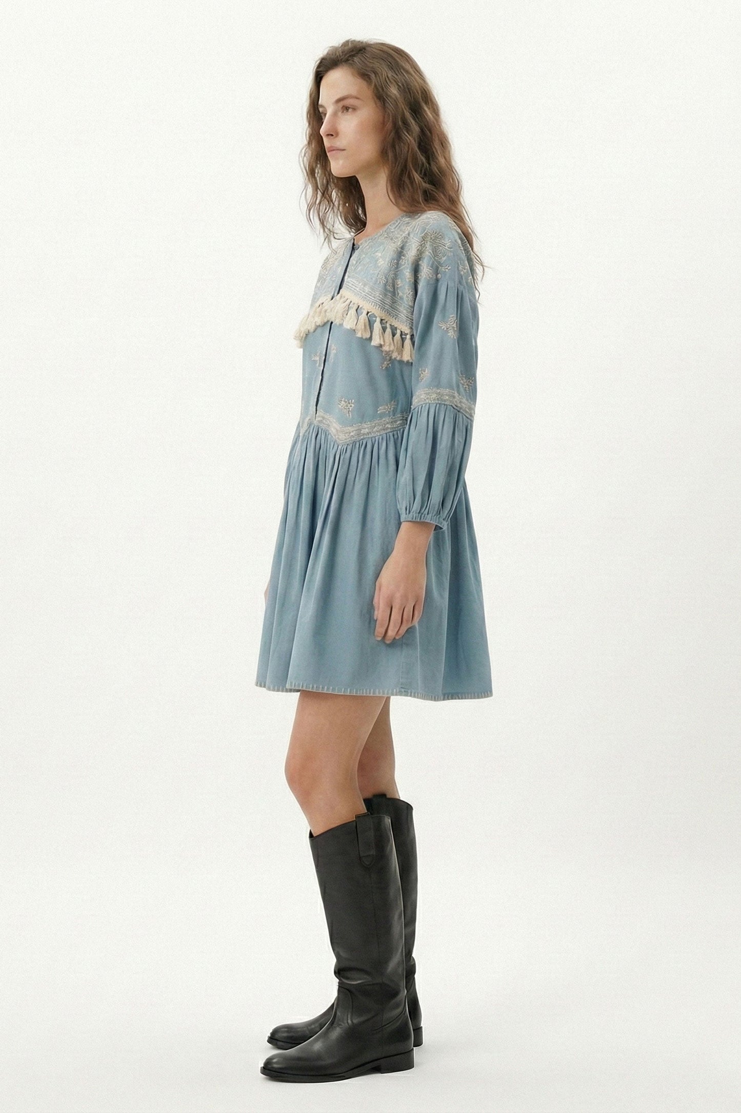 Woman wearing a light blue dress with lace details and black boots on a white background