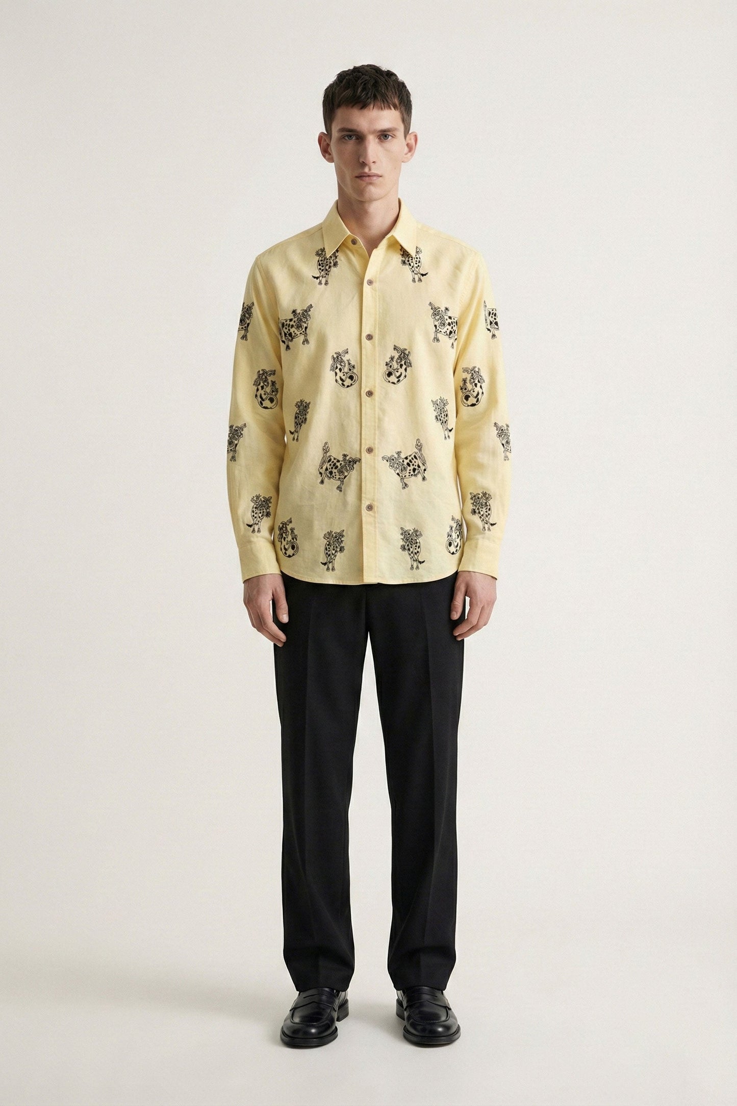 Man wearing a yellow patterned shirt with black pants on a white background