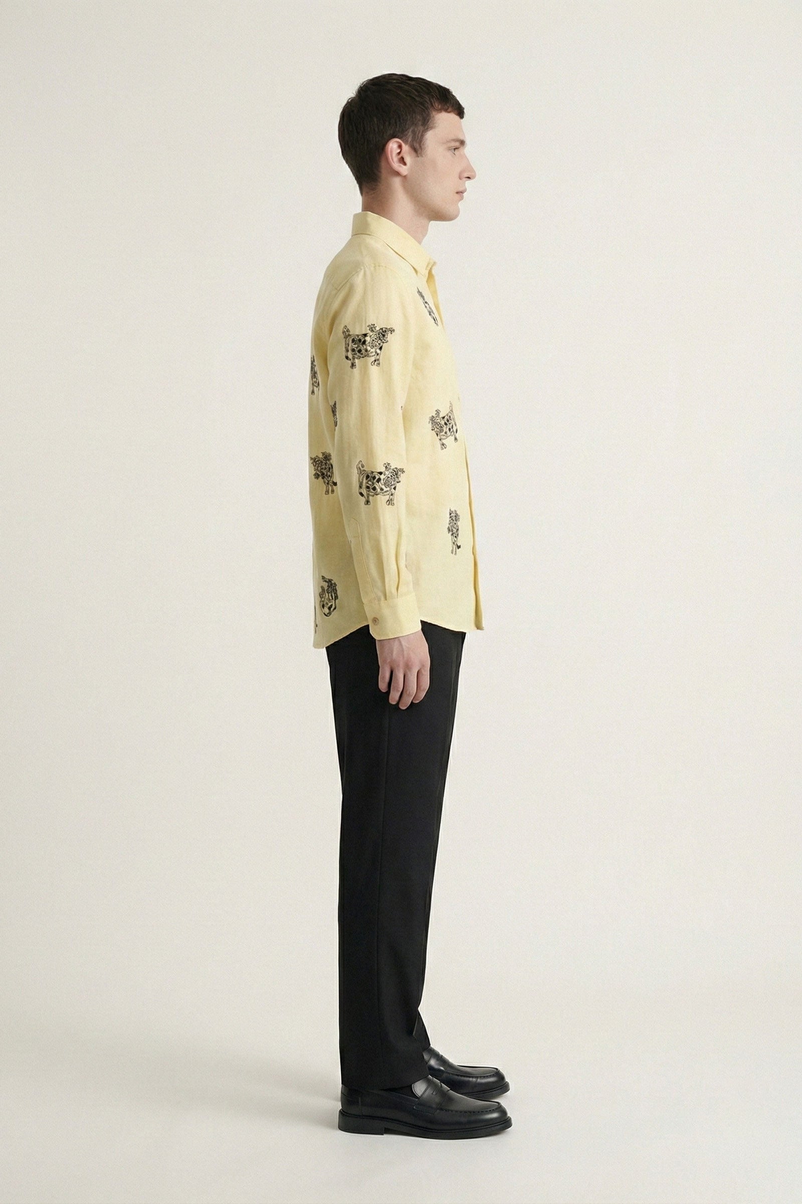 Man wearing a light yellow patterned shirt and black pants on a white background
