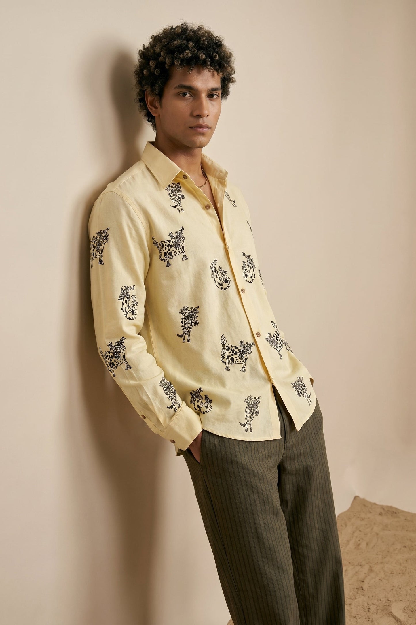 Man wearing a light-colored shirt with floral patterns against a beige wall.