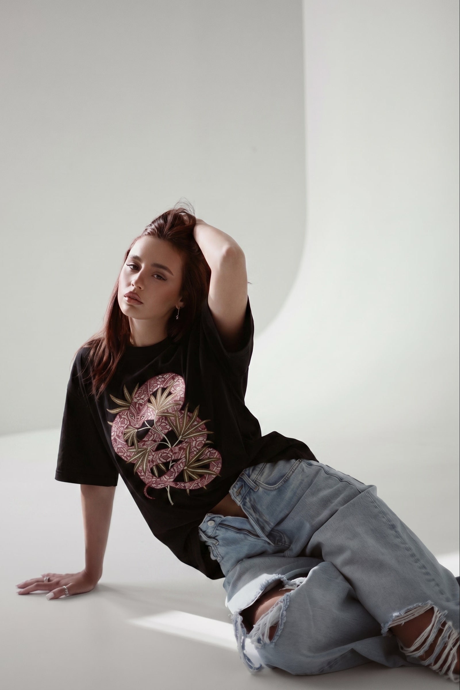 Person wearing a black t-shirt with a pink graphic design and light blue jeans on a white background