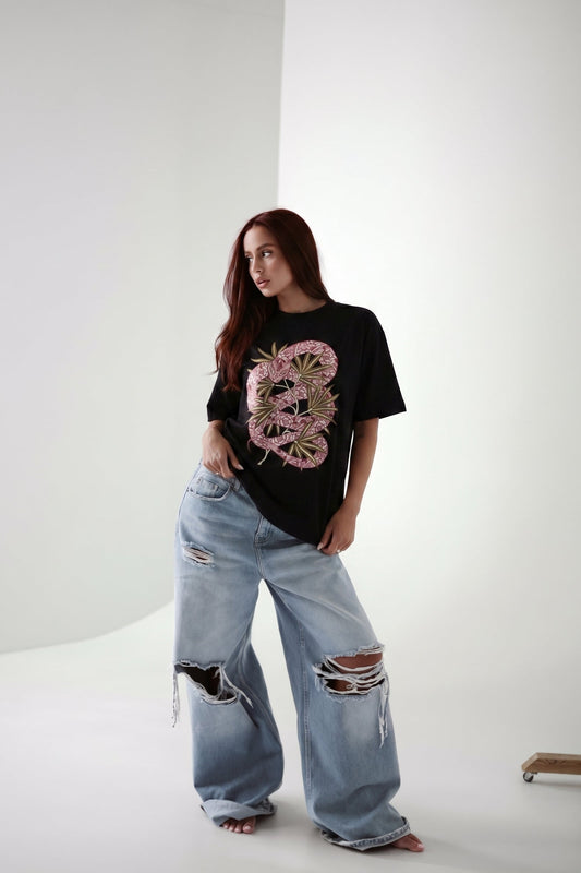 Person wearing a black t-shirt with a pink floral design and light blue jeans on a white background