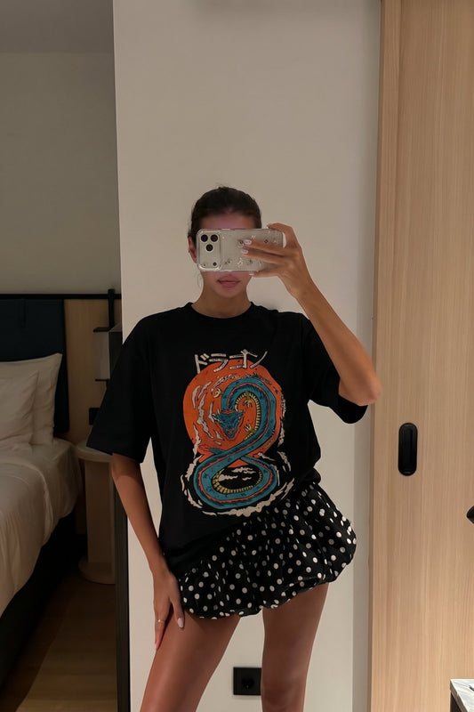 Person taking a mirror selfie wearing a black graphic t-shirt and polka dot shorts in a room.