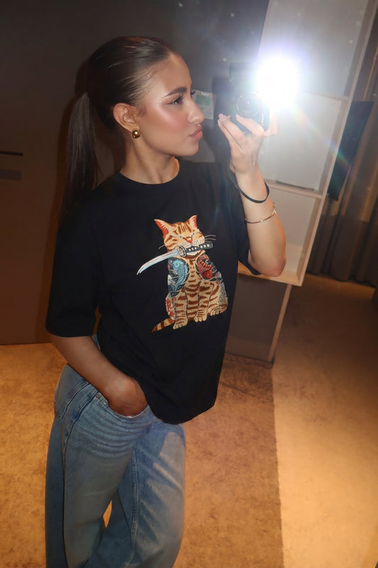 Person wearing a black t-shirt with a cat graphic design in a room.