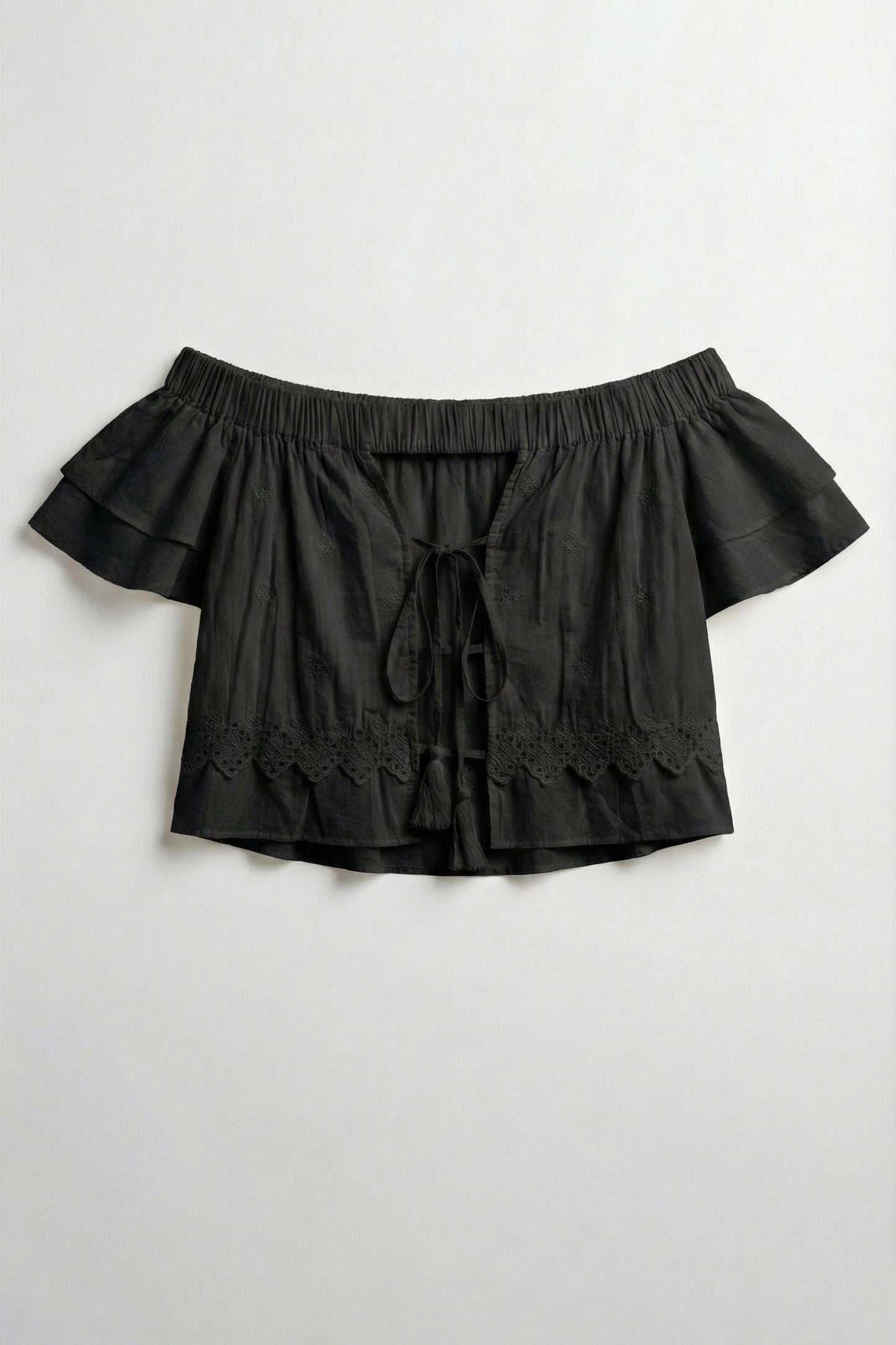 Black off-shoulder top with ruffled details on a light gray background