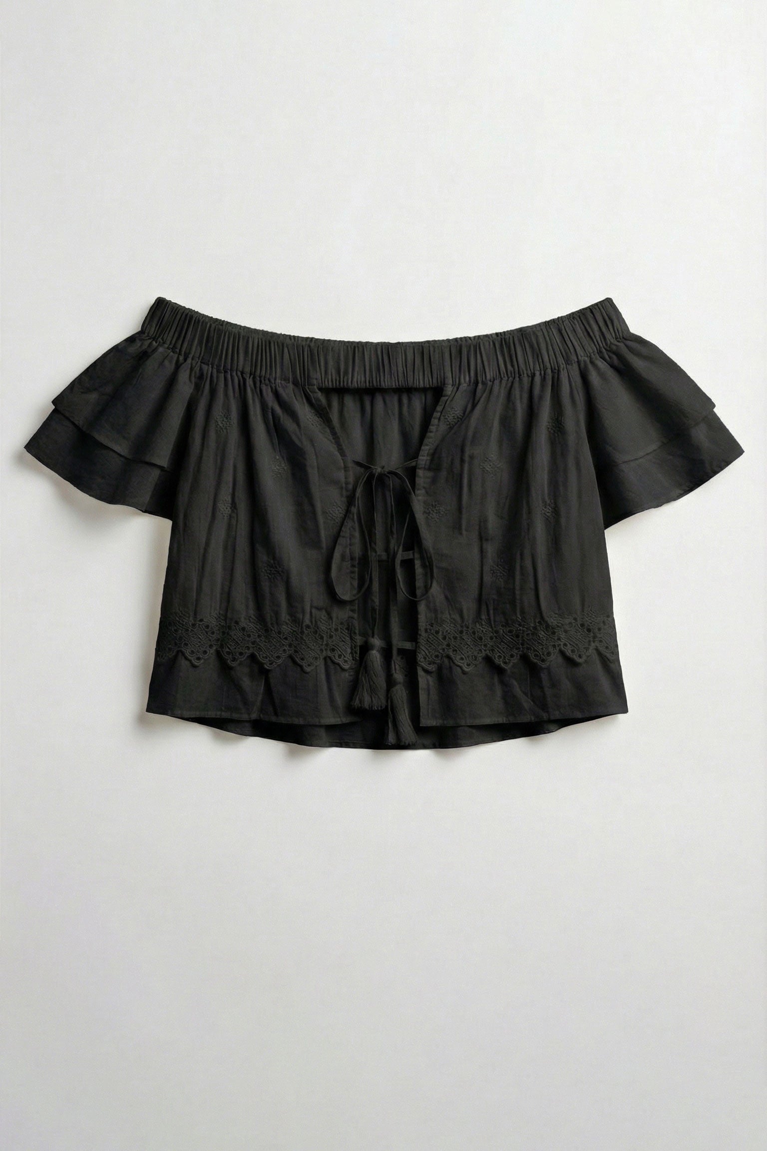 Black off-shoulder top with ruffled details on a light gray background