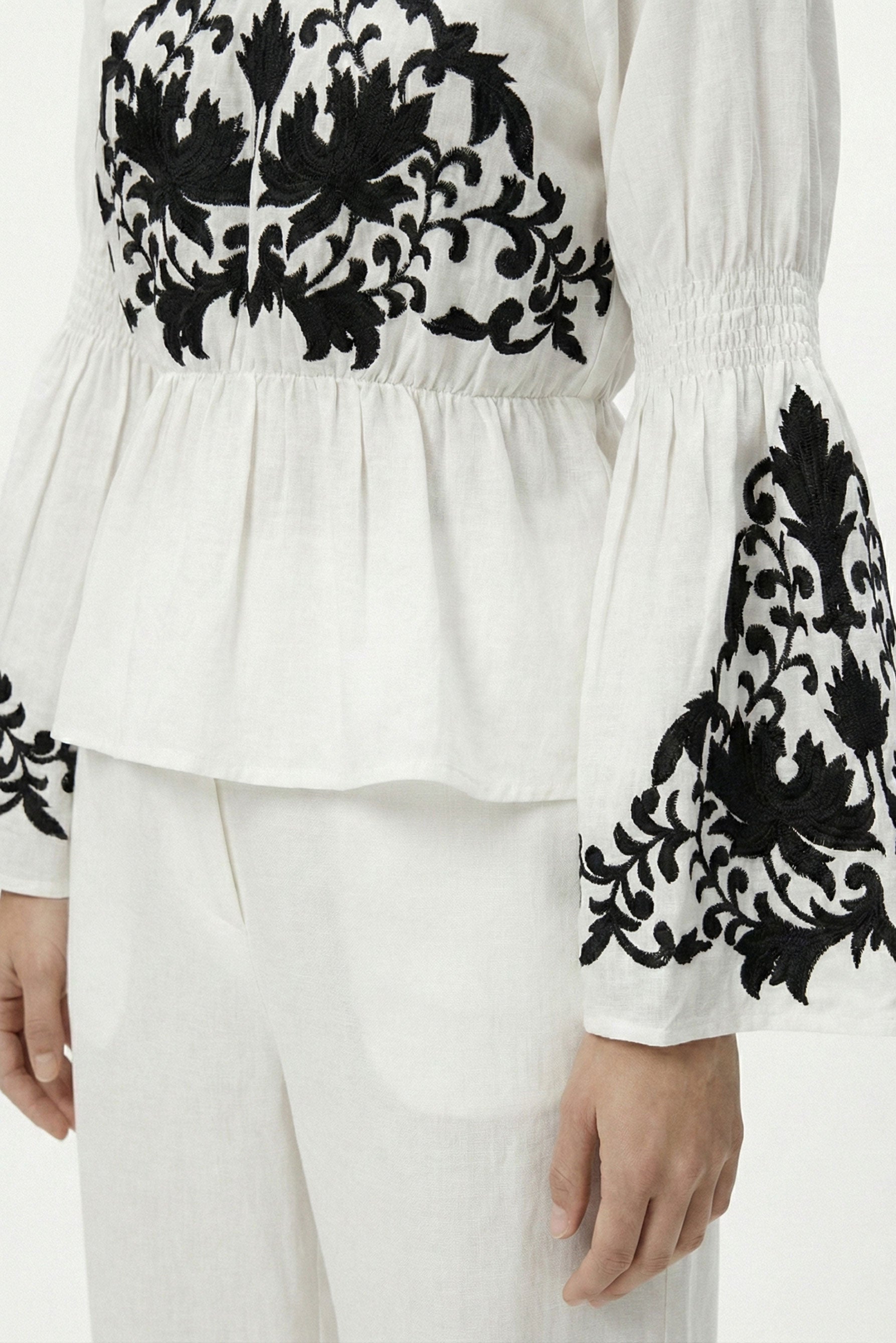 White blouse with black floral embroidery on sleeves and neckline against a white background