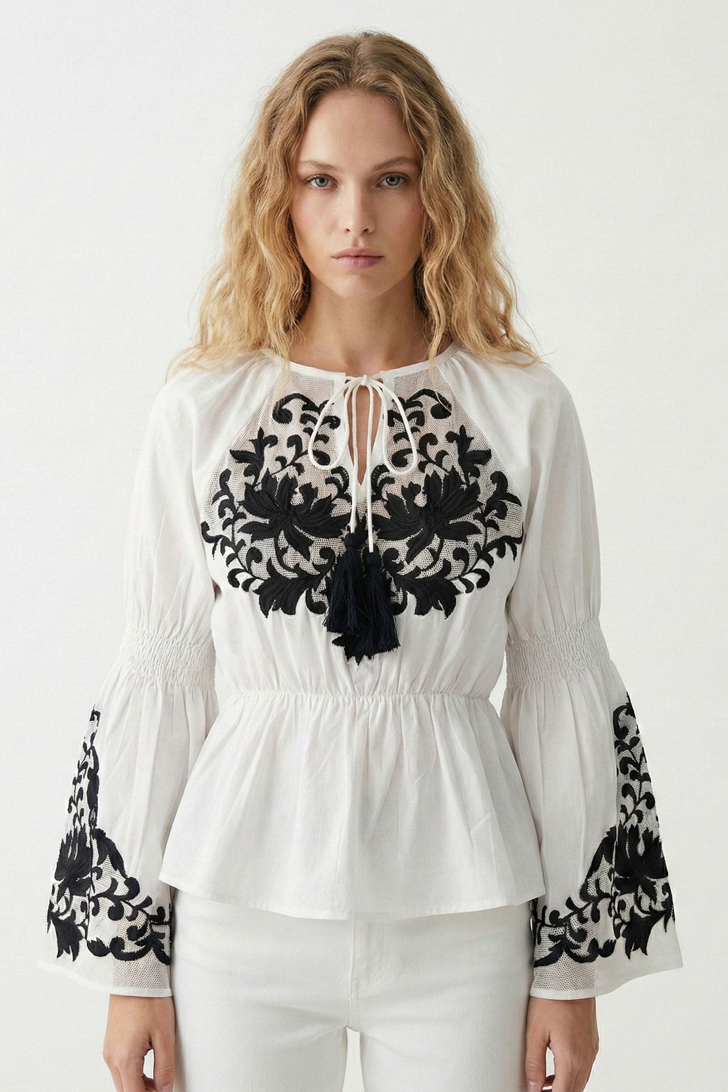 Woman wearing a white blouse with black lace details on a white background