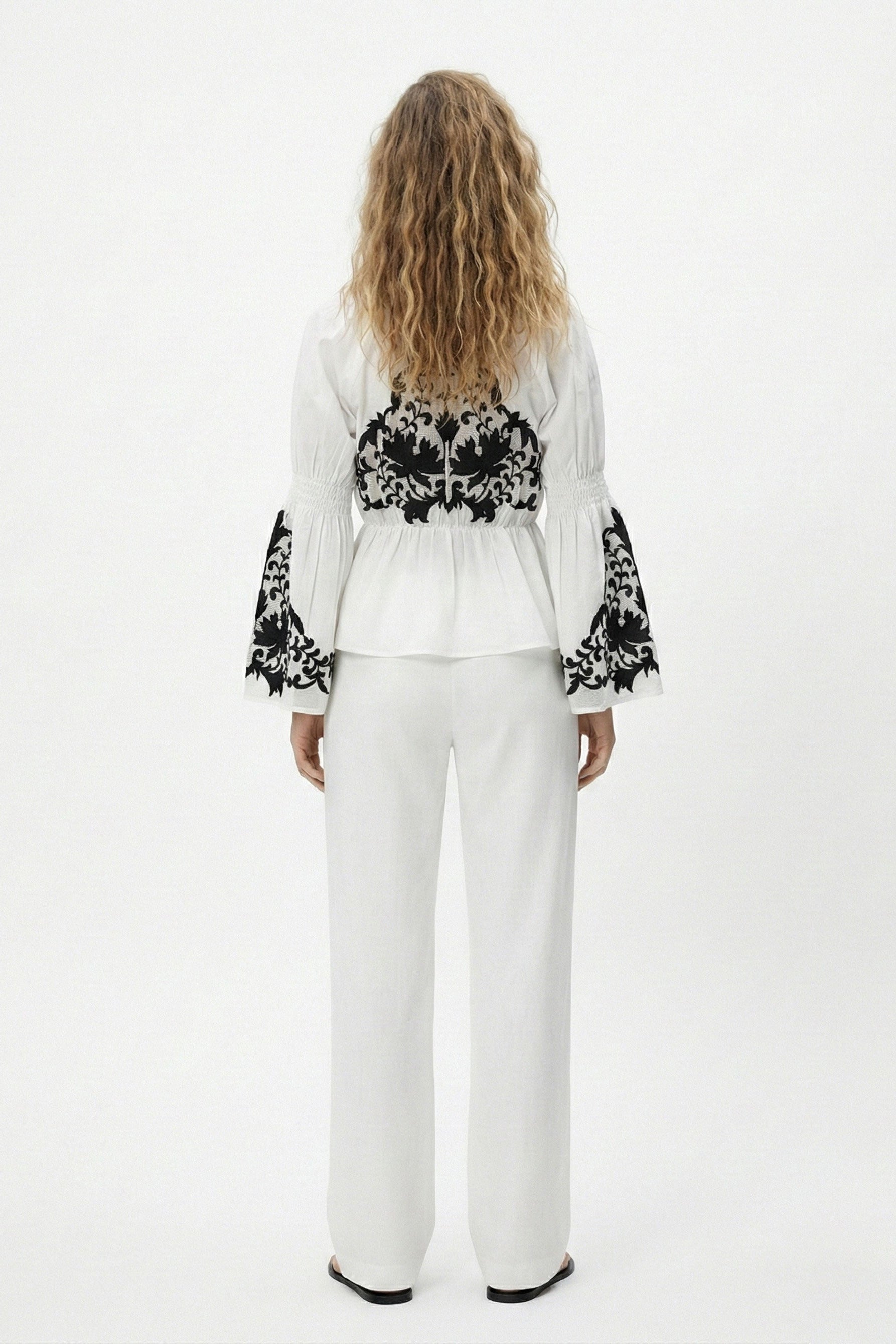 Woman wearing a white outfit with black floral patterns on a white background