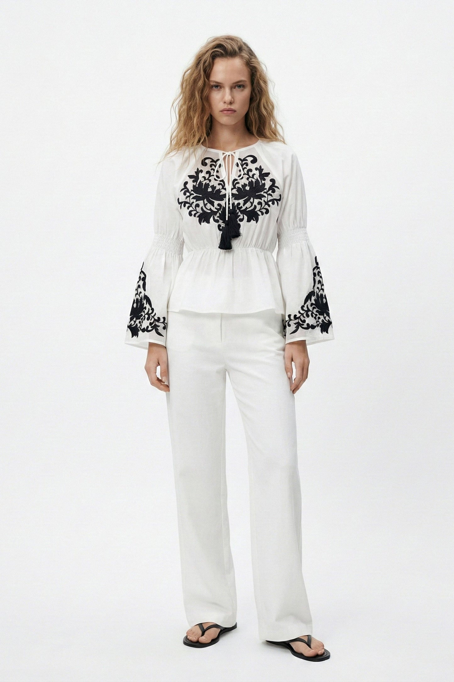 Woman wearing a white outfit with black embroidery on a white background