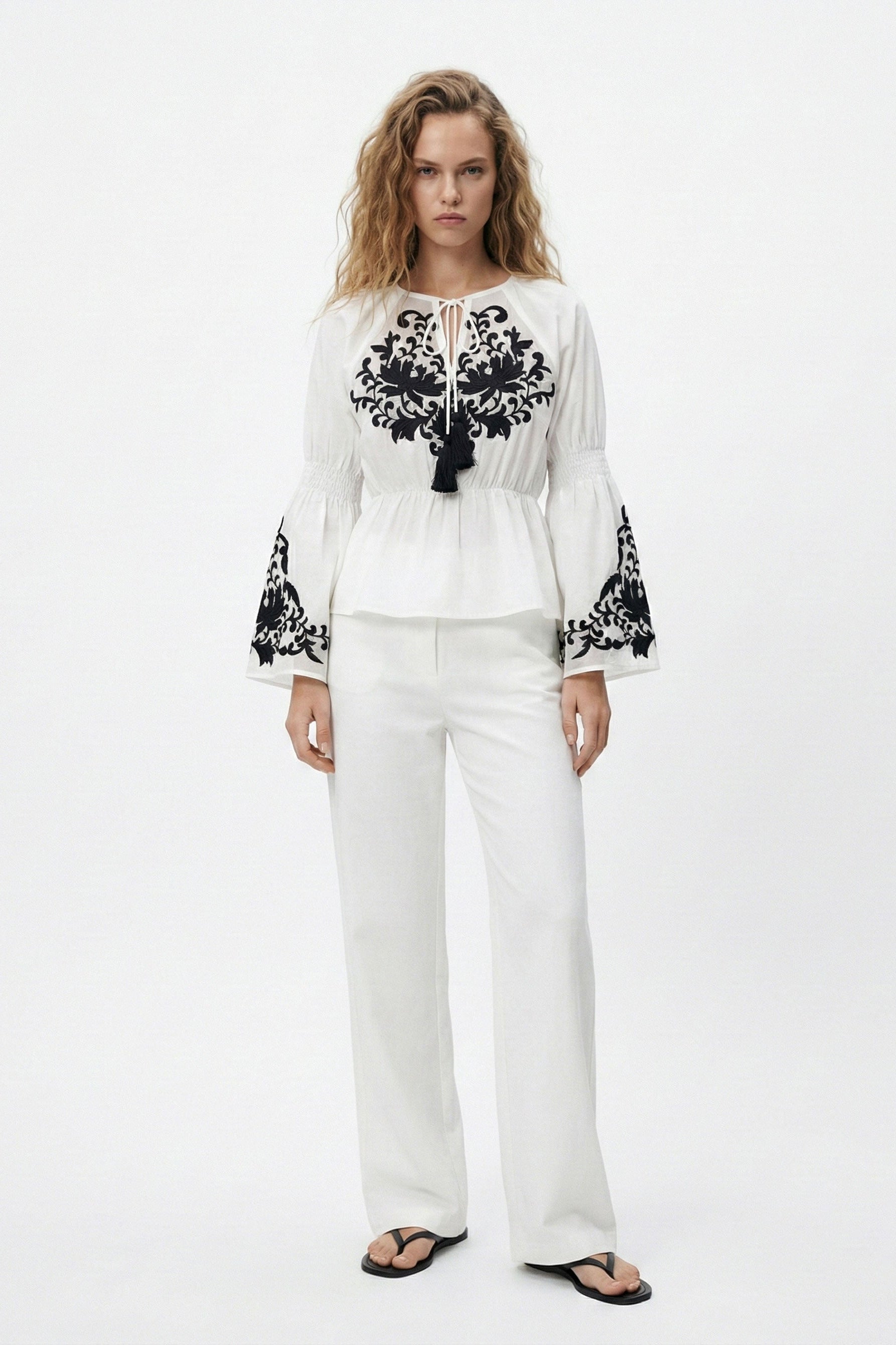 Woman wearing a white outfit with black embroidery on a white background