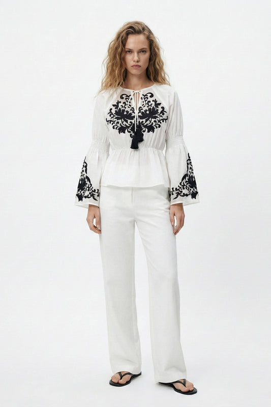 Woman wearing a white outfit with black embroidery on a white background